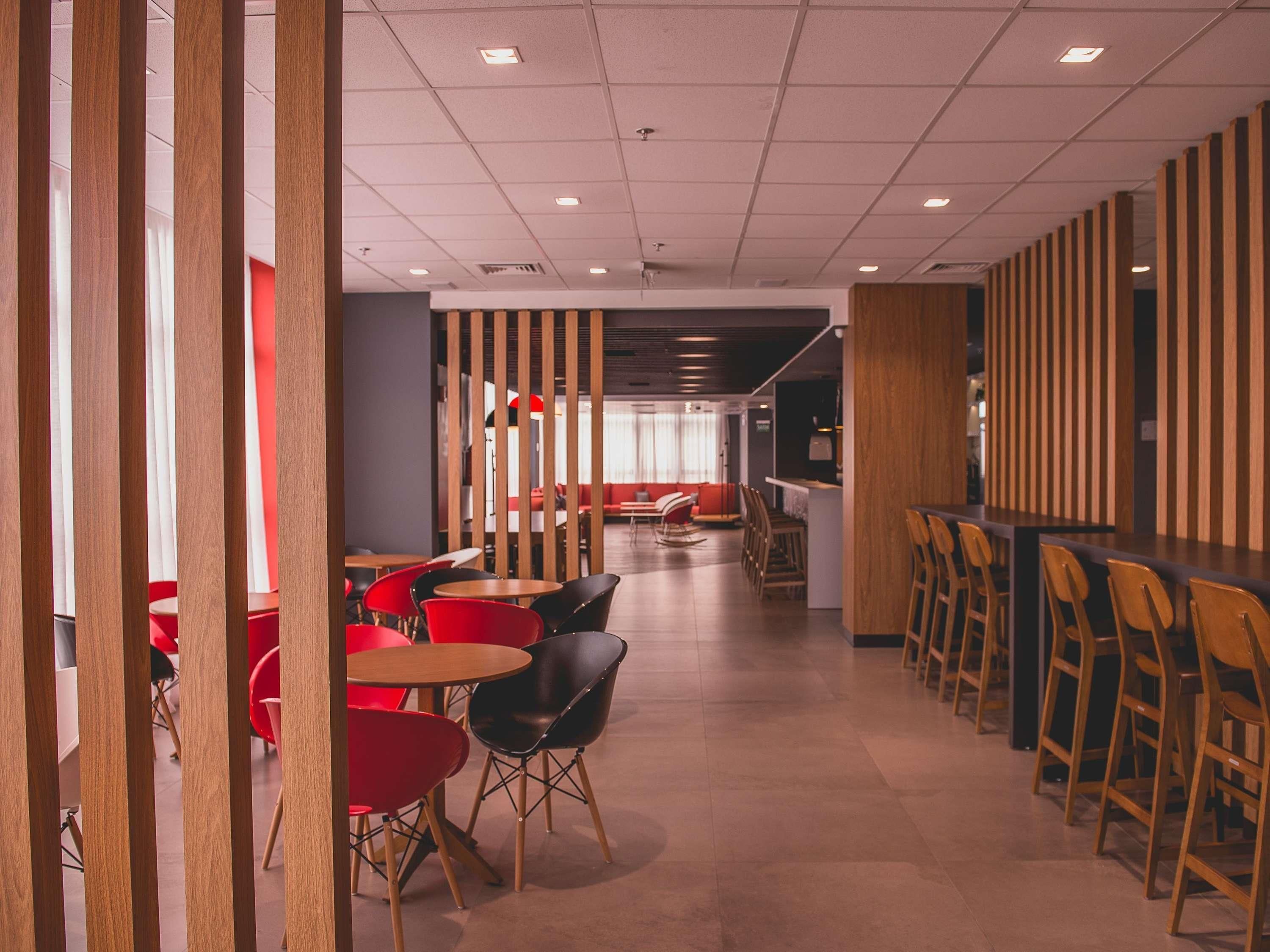 A modern interior with a long counter, red and black chairs, and a seating area with red sofas.