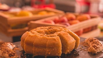 A bundt cake on a dark slate plate with a chocolate drizzle, surrounded by fruits and a blurred background.
