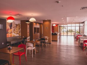 A modern restaurant interior with wooden flooring, red and white chairs, and pendant lighting. - Ibis Carlos Barbosa (Carlos Barbosa)