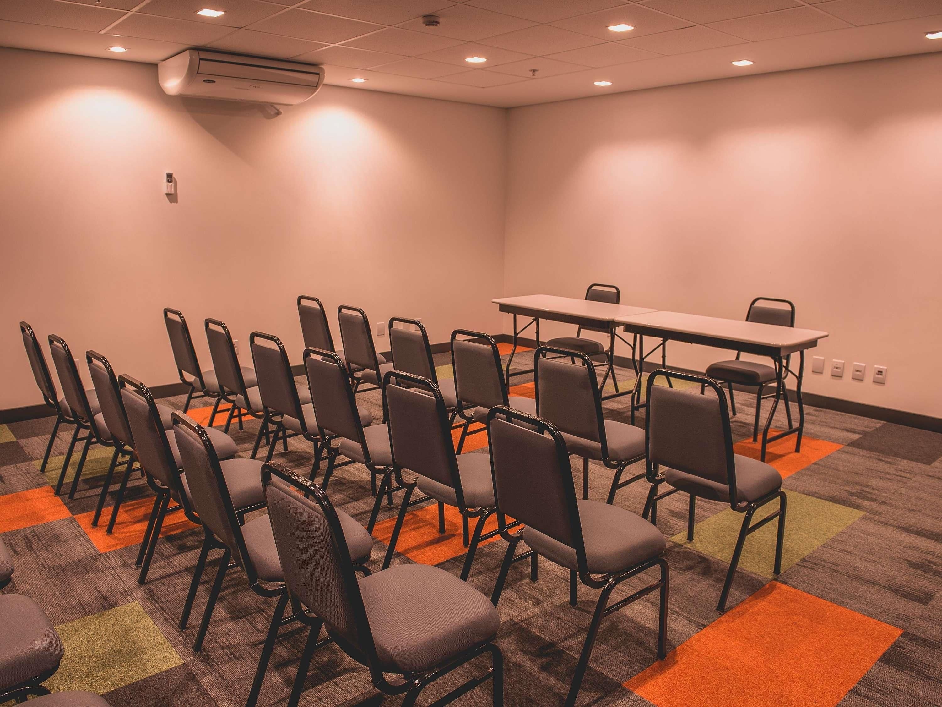 Konferenssihuone, jossa on riveissä tuoleja, pöytä ja ilmastointilaite.