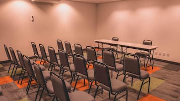 Konferenssihuone, jossa on riveissä tuoleja, pöytä ja ilmastointilaite.