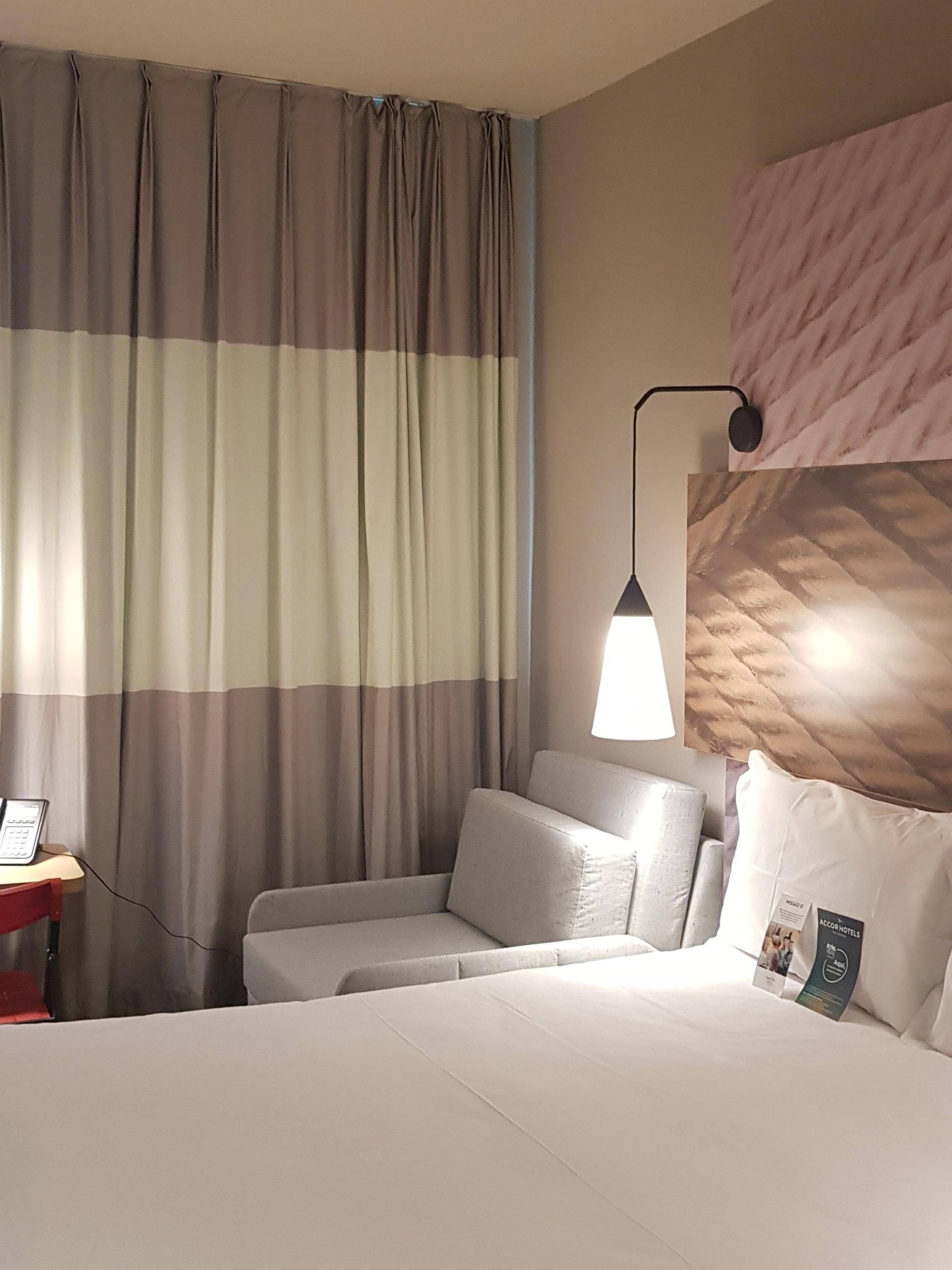 A hotel room with a bed, a bedside table with a phone, a lamp, and a headboard with a patterned design.