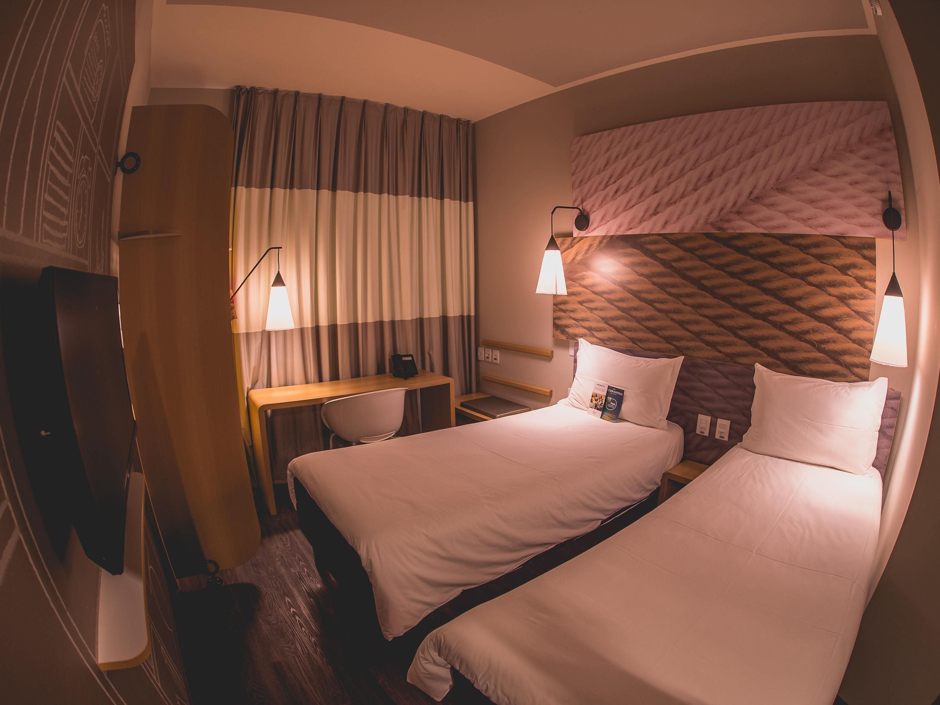 A hotel room with two beds, a desk, a chair, and a minibar.