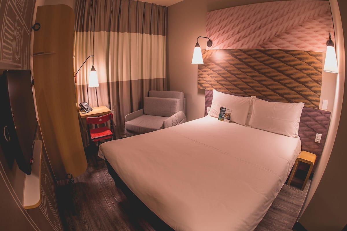 Une chambre dâhĂŽtel avec un lit, un bureau, une chaise, une lampe et un rideau.