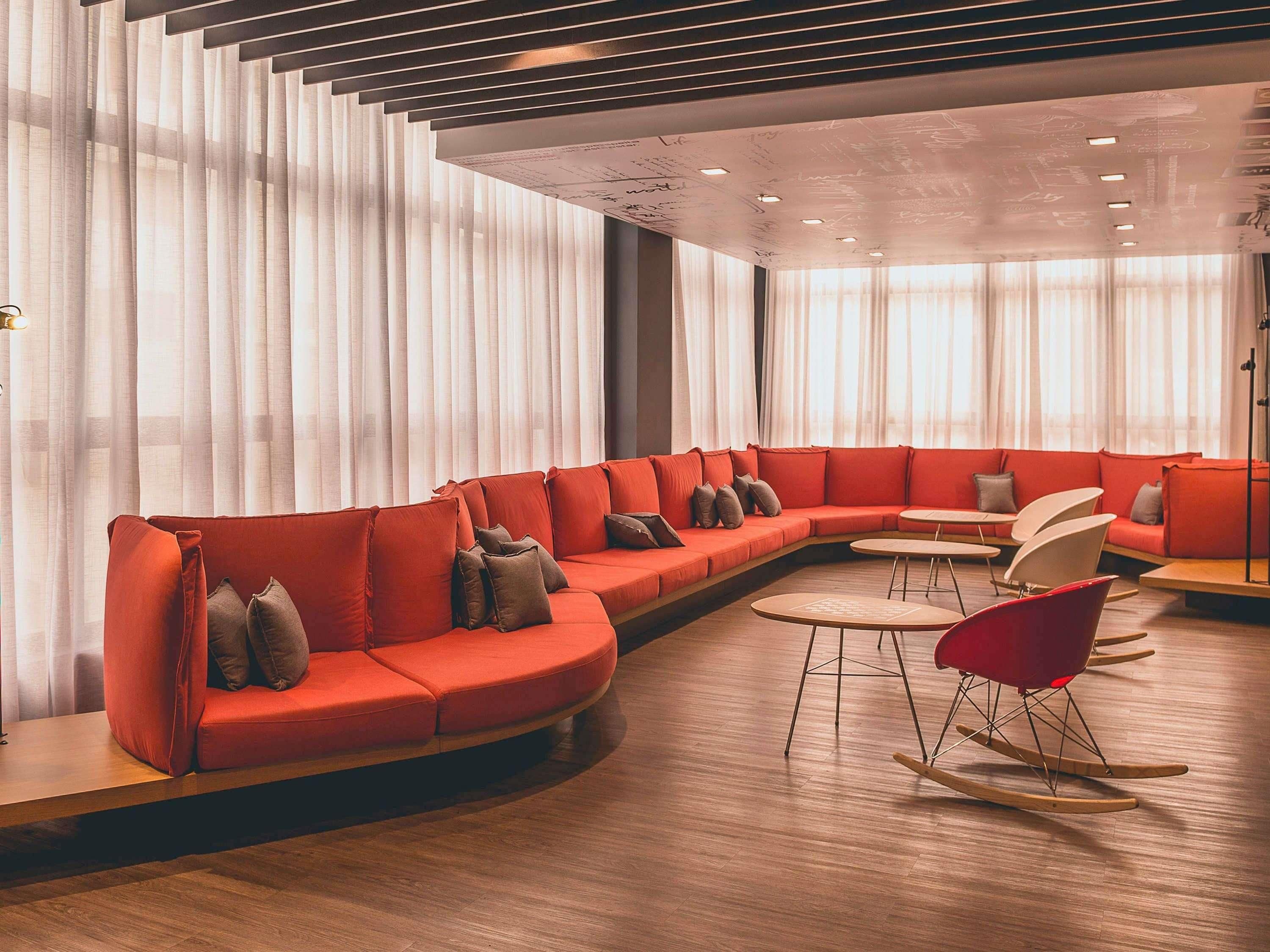 A modern lounge area with a curved red sofa, small round tables, and a rocking chair.