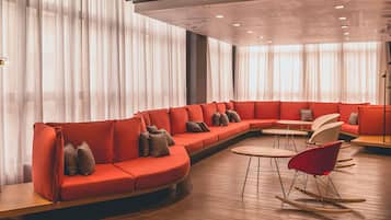 A modern lounge area with a curved red sofa, small round tables, and a rocking chair.