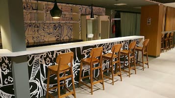 Uma área de bar com um balcão comprido, vários banquinhos de madeira e uma parede com padrões abstratos em preto e branco.