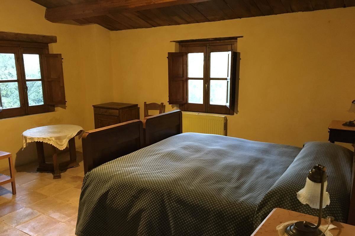 A room with a bed, a small table, a chair, and a window with wooden shutters.