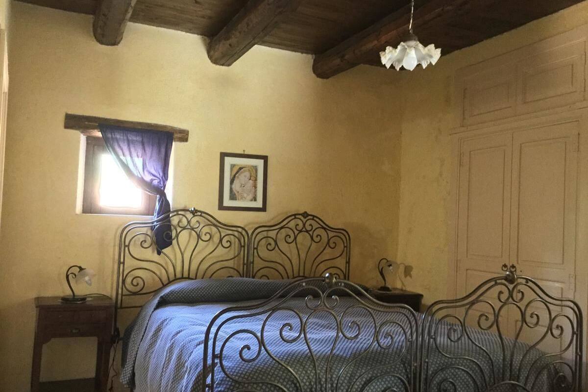 A bedroom with a metal bed frame, a bedside table with a lamp, a window with a curtain, and a framed picture on the wall.