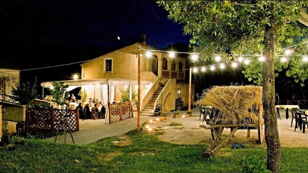 A rustic outdoor dining area with a staircase leading to a covered terrace, string lights, and a hay bale decoration. - Agriturismo Colloreto (Morano Calabro)