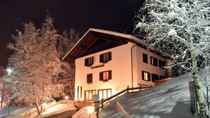 Un edifici de diversos pisos amb teulada inclinada, envoltat d'arbres coberts de neu i una pendent nevada.