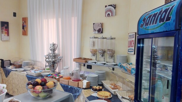 A buffet setup with various food items, a beverage dispenser, and a refrigerator labeled 'Santal'. - Hotel Fiore (Fiorenzuola d'Arda)