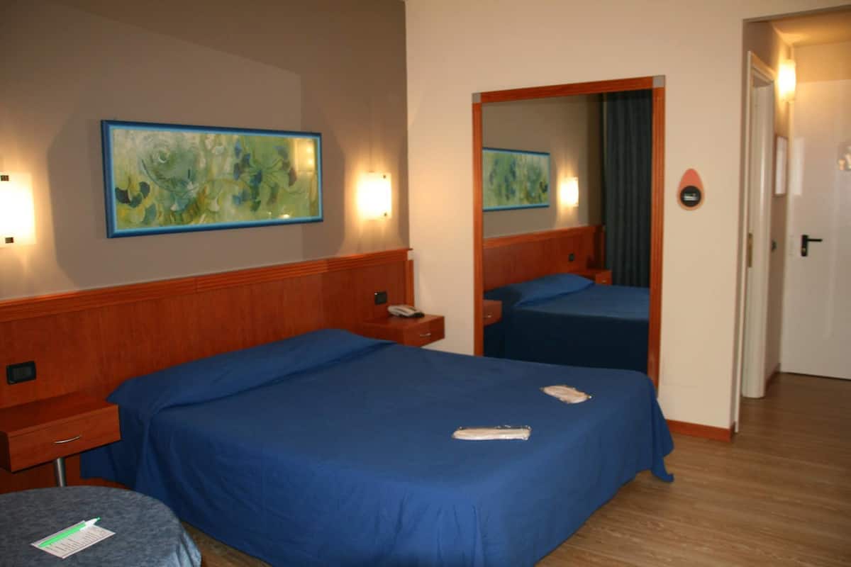 A hotel room with two beds, a wooden headboard, a bedside table with a phone, and a wall-mounted painting.