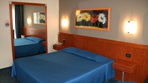 A hotel room with two beds, a bedside table with a lamp, a painting on the wall, and a mirror. - Hotel Fiore (Fiorenzuola d'Arda)