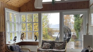 A cozy room with wooden walls and ceiling, large windows, a sofa, chairs, and a table. - Kaldbaks-kot Cottages  (Husavik)