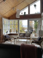 Una habitación acogedora con paredes y techo de madera, ventanas amplias, un sofá, sillas y una mesa.