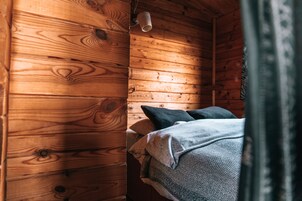 Interior de una cabaña de madera con una cama, almohadas y una lámpara colgante.