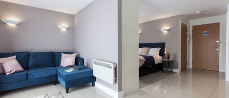 Una habitación de hotel moderna con un sofá azul, una cama, una mesita auxiliar pequeña y un radiador blanco.