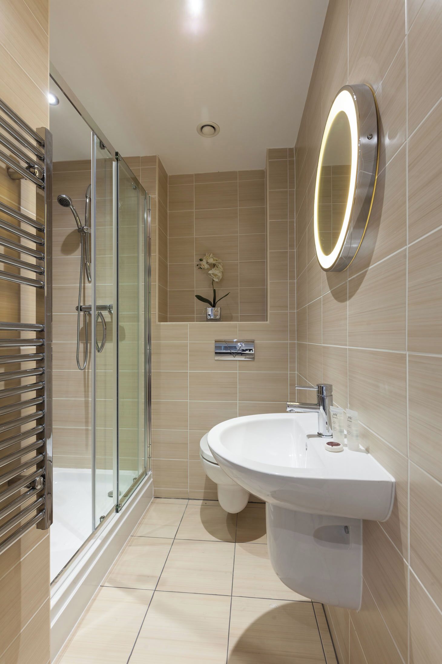 A modern bathroom with a glass-enclosed shower, a white sink, and a mirror with a lighted frame.