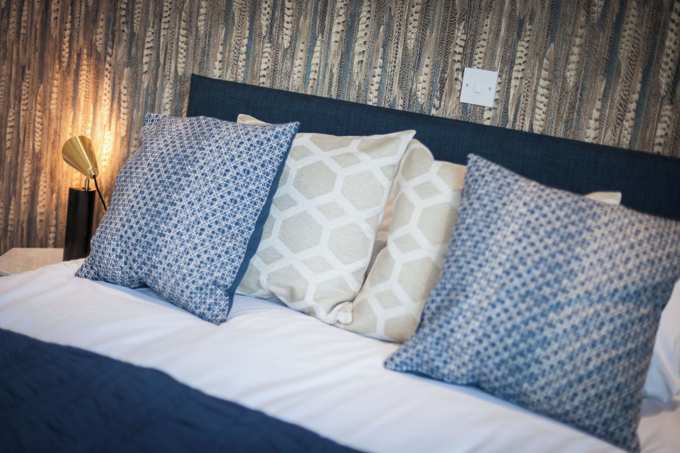 A neatly made bed with patterned pillows and a headboard against a textured wall.