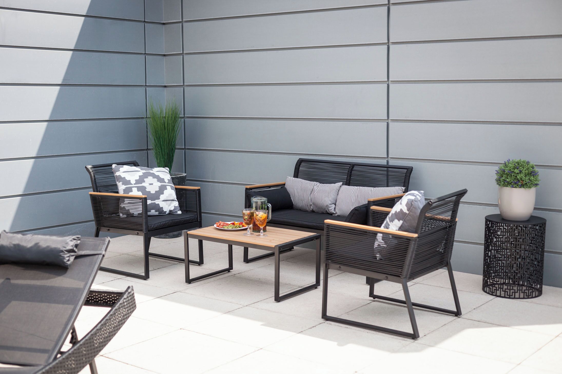 An outdoor seating area with a sofa, two chairs, a small table, and a potted plant.