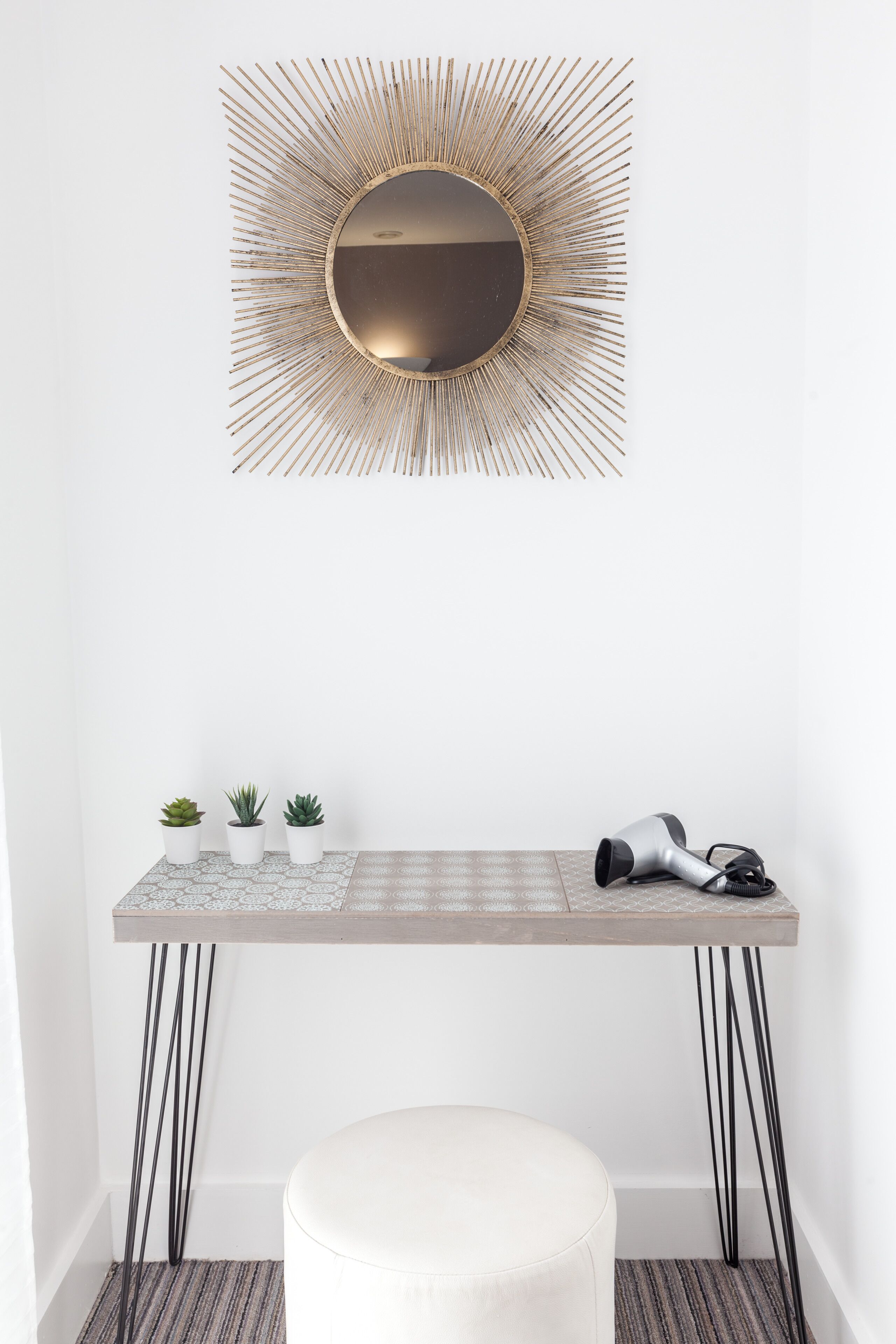 A modern vanity with a sunburst mirror, a small table with potted plants, and a hairdryer.
