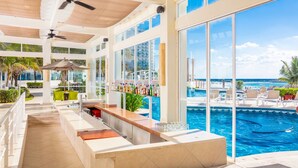 A poolside bar area with a view of the ocean, a bar counter, and a ceiling fan. - Krystal Cancun All Inclusive (Cancun)