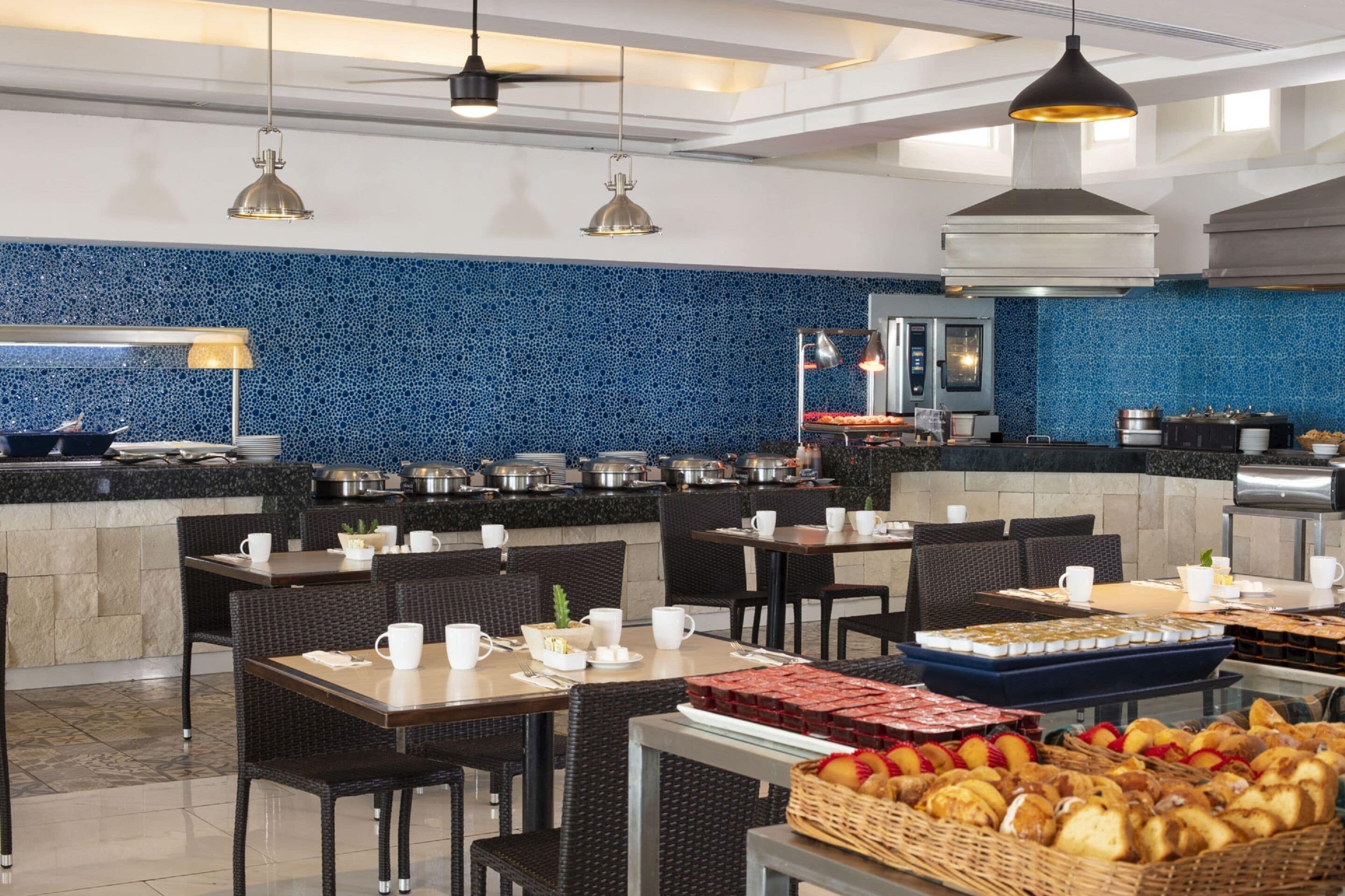 Un comedor espacioso con varias mesas y sillas, una barra de buffet y un salpicadero de azulejos azules.