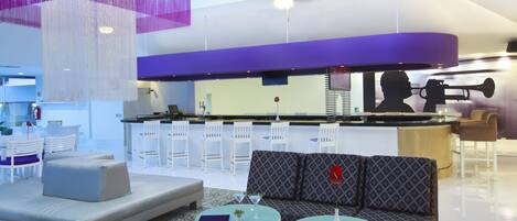 A modern lounge area with a sofa, two round tables, and a bar area with white chairs.