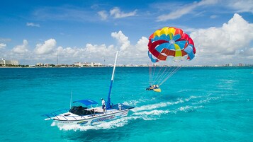 A speedboat with a parasail and a person parasailing over turquoise water.