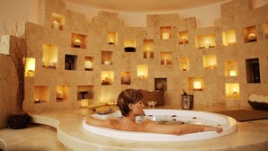 A spa room with a large bathtub, a wall with multiple small windows, and a vase with dried branches. - Krystal Cancun All Inclusive (Cancun)