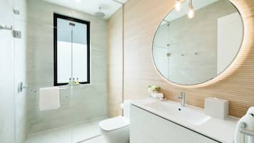 Een moderne badkamer met een douchecabine van glas, een ronde spiegel, een witte wastafel en een toilet.