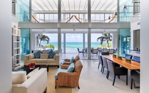 A spacious lobby with a view of the ocean, a seating area with a sofa and chairs, and a dining table with chairs. - Villas at Blue Mountain  (Providenciales)