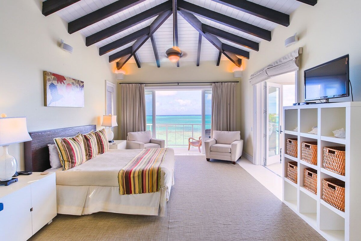 A hotel room with a bed, two armchairs, a TV, and a view of the ocean.