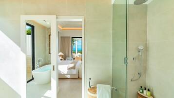 A modern bathroom with a glass shower enclosure, a bathtub, and a visible bedroom with a bed and curtains.