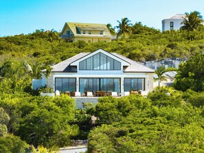 A modern two-story house with large windows, surrounded by lush greenery and a hill. - Villas at Blue Mountain  (Providenciales)