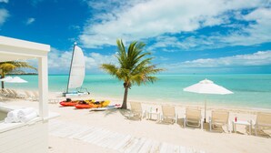 Een strand met witte ligbedden, een zeilboot en een palmboom.
