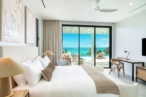 A modern hotel room with a large bed, a desk, and a view of the ocean. - Bespoke Villas Turks and Caicos (Providenciales)