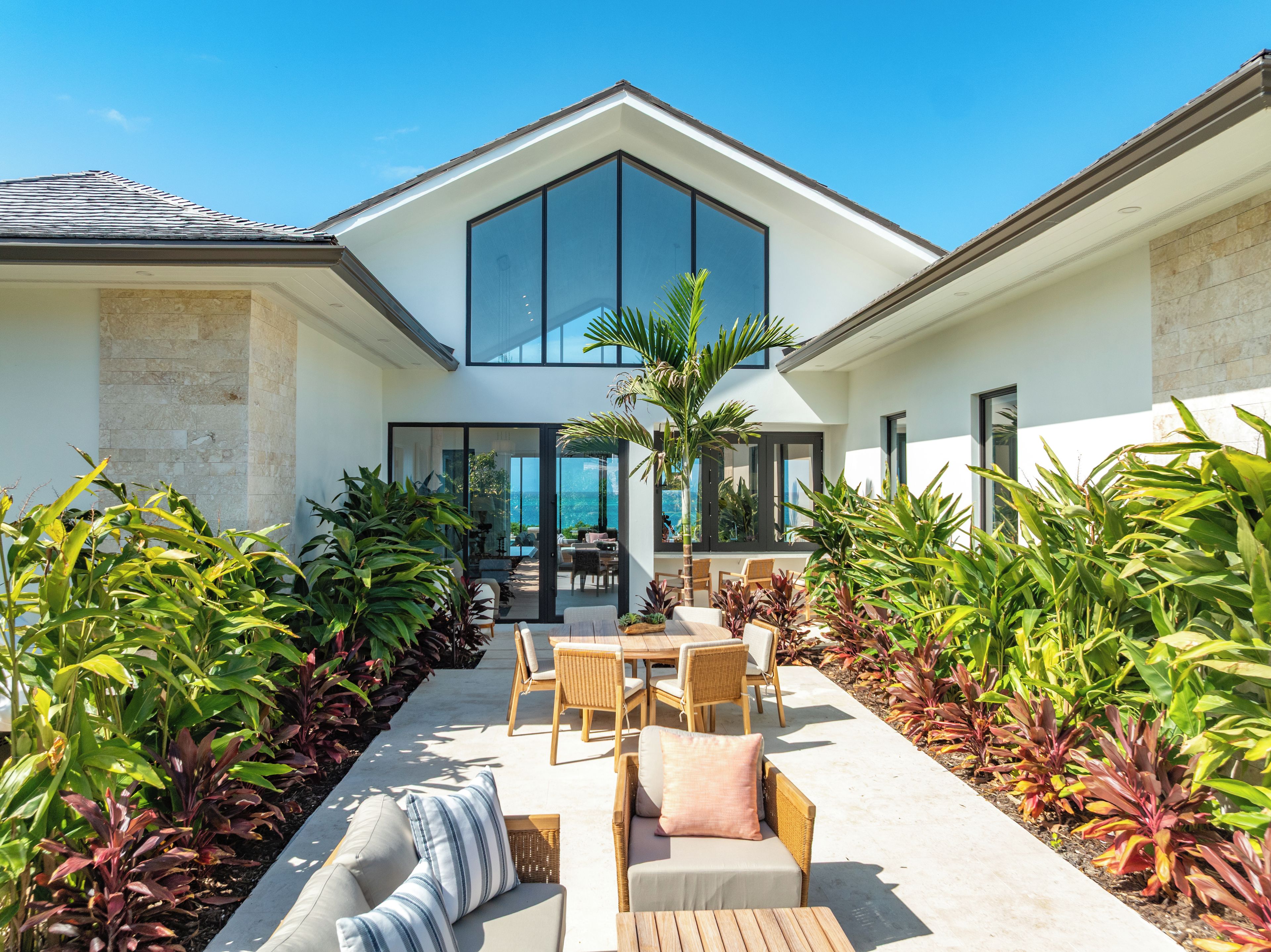 Une maison moderne dotée d’un patio aménagé avec du mobilier d’extérieur et une végétation luxuriante.