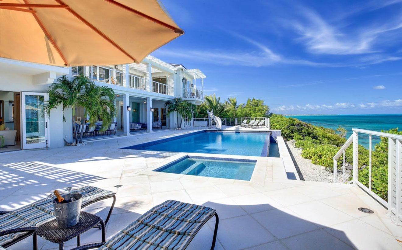 Un espace aménagé au bord de la piscine, avec des chaises longues, un jacuzzi et une vue sur l’océan.