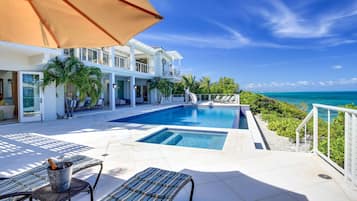 Un espace aménagé au bord de la piscine, avec des chaises longues, un jacuzzi et une vue sur l’océan.