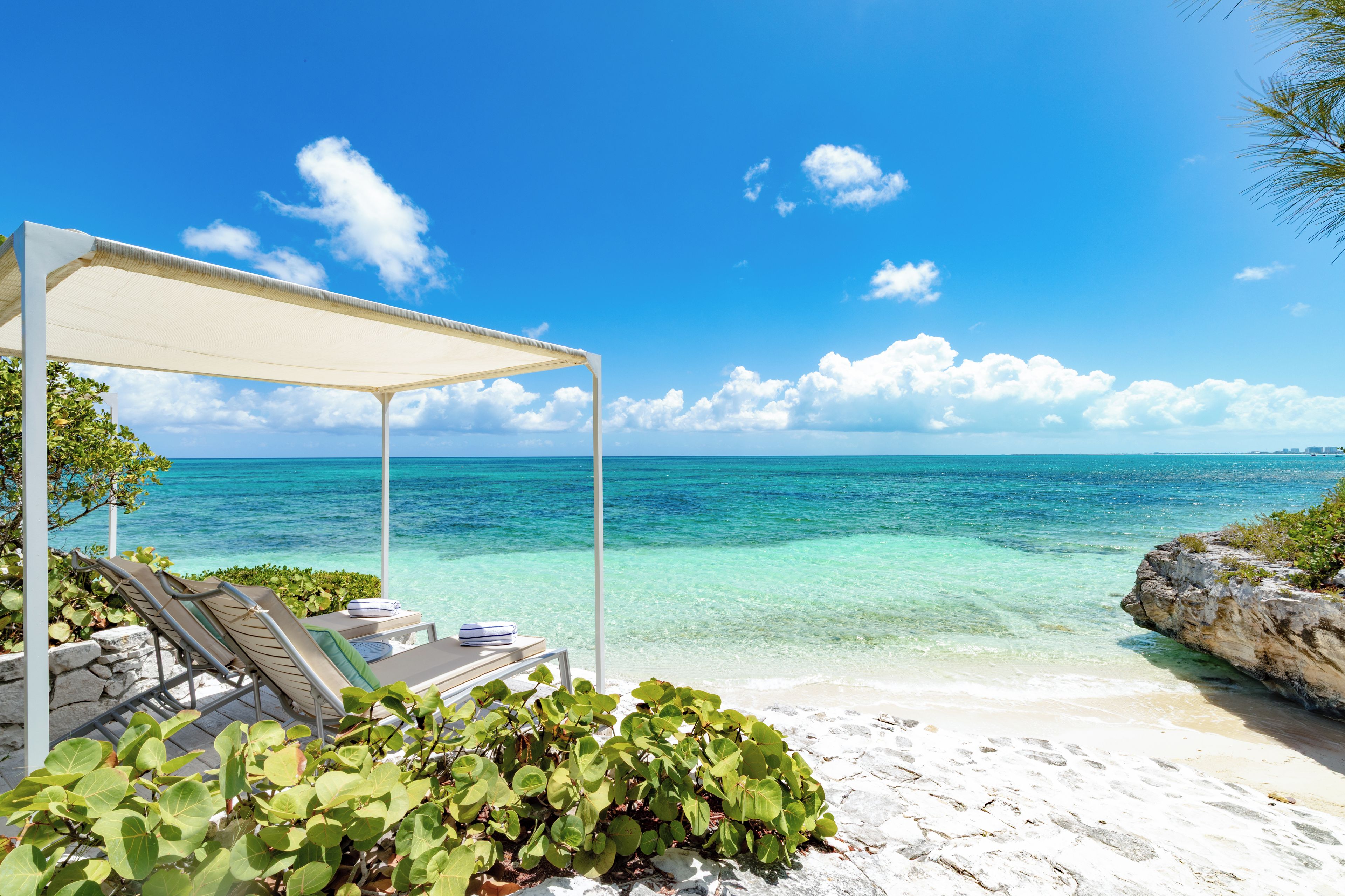 Een strand met helder turquoise water, een wit zandstrand en een overdekt loungegedeelte met uitzicht op zee.