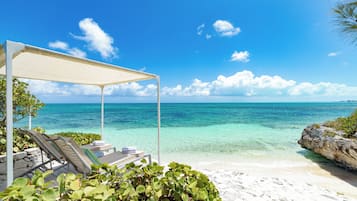 Een strand met helder turquoise water, een wit zandstrand en een overdekt loungegedeelte met uitzicht op zee.