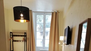 A bedroom with a bed, a wooden chair, a desk, a TV, a coat rack, and a window with curtains. - Hotel Saint Daniel (Nantes)