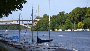 A marina with several boats docked along the shore, a bridge in the background, and a forested hillside. - Hotel Saint Daniel (Nantes)