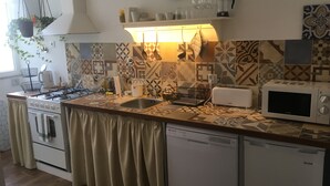 A kitchen with a gas stove, oven, sink, and a microwave. There is a clock on the wall and a hanging plant. - Casa do Peso (Peso da Régua)