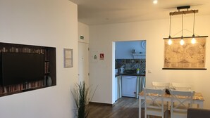 A modern living room with a flat-screen TV, a dining area with white chairs, a kitchen with a map on the wall, and a potted plant. - Casa do Peso (Peso da Régua)