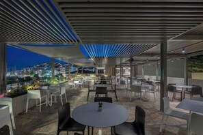 An outdoor dining area with tables and chairs, a view of the cityscape, and a modern architectural ceiling design. - Alkyon (Skiathos)