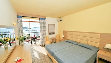 A hotel room with a large bed, a wooden desk, a chair, and a view of the sea.