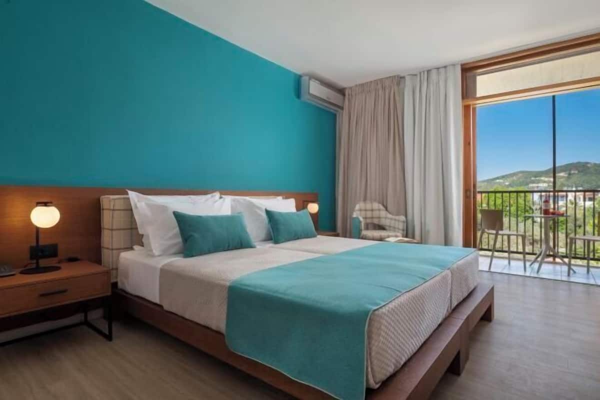 A hotel room with a bed, a nightstand, a chair, and a balcony with a view.